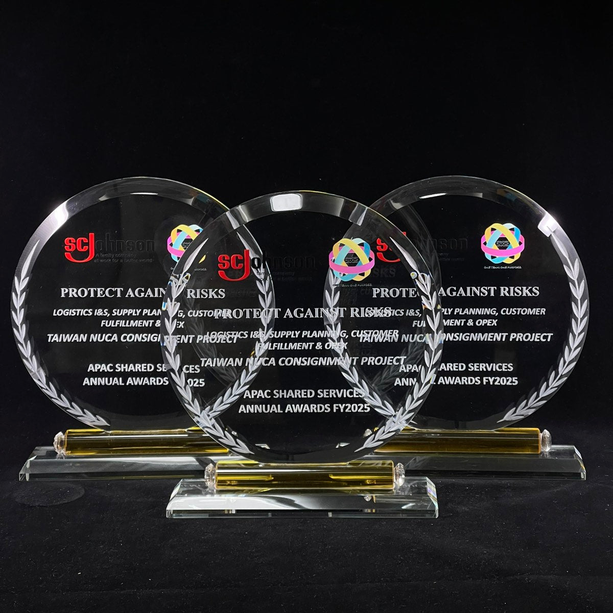 Three round glass awards with text and logos on a black background