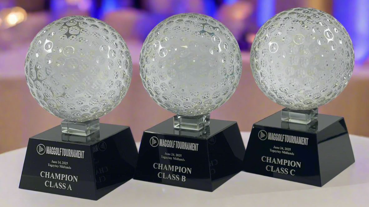 Three crystal golf ball trophies on black bases with 'Maggolf Tournament' branding.
