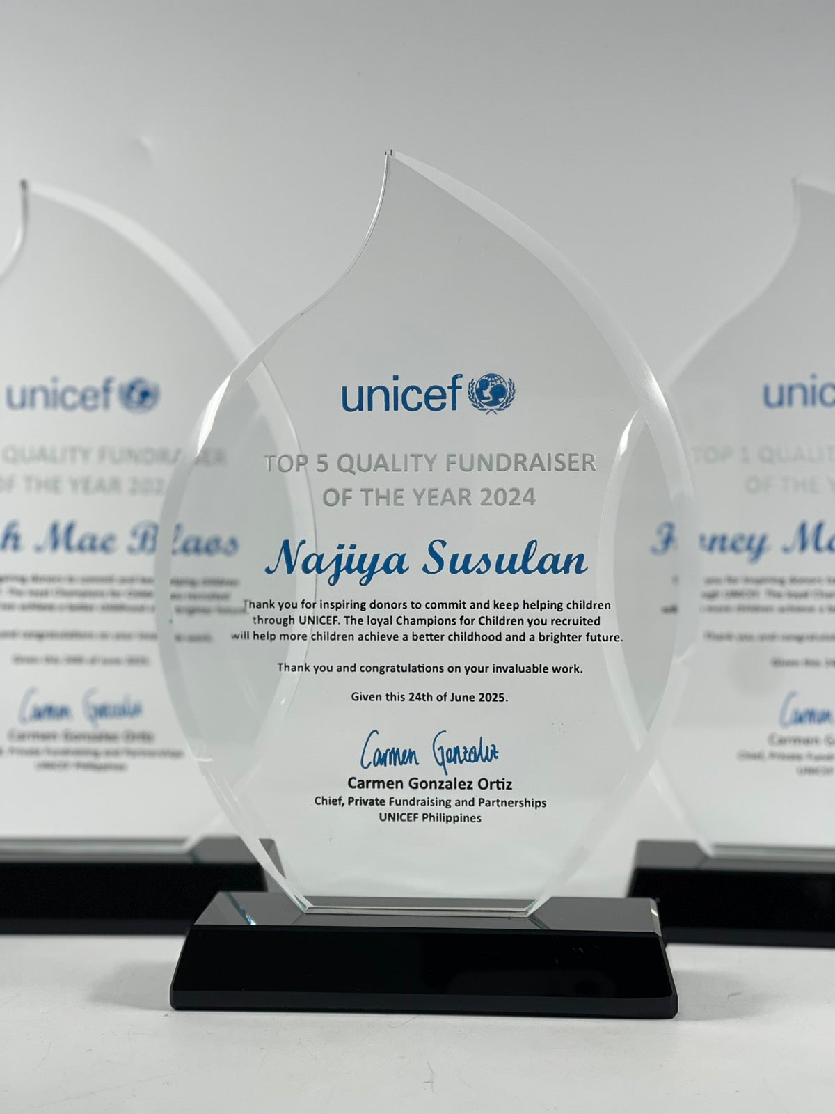 UNICEF award for Top 5 Quality Fundraiser of the Year 2024 to Najia Susulan, with a clear glass award and black base.