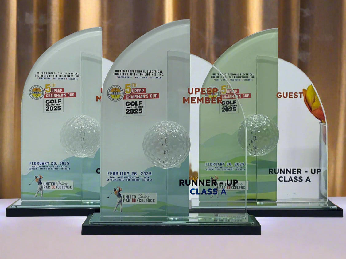 Four glass awards with text and a golf ball design on a white background